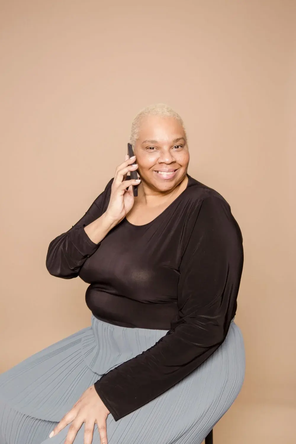 A smiling woman talking on her phone against a warm beige background